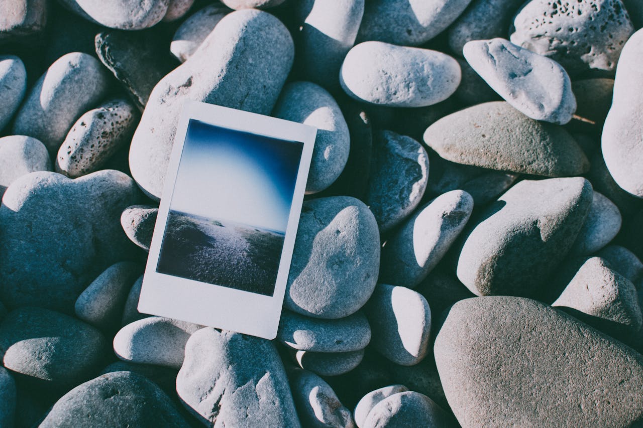 Polaroid photo placed on smooth pebbles on a beach, showcasing a serene nature scene.