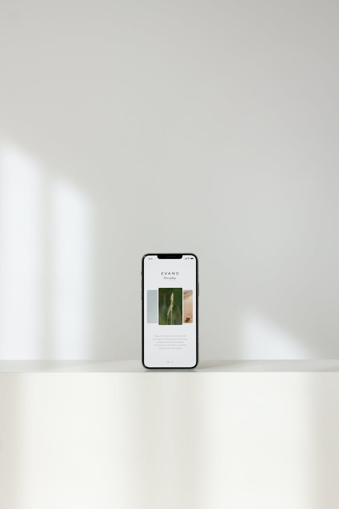 A sleek smartphone displaying a modern website, on a white shelf with a serene background.